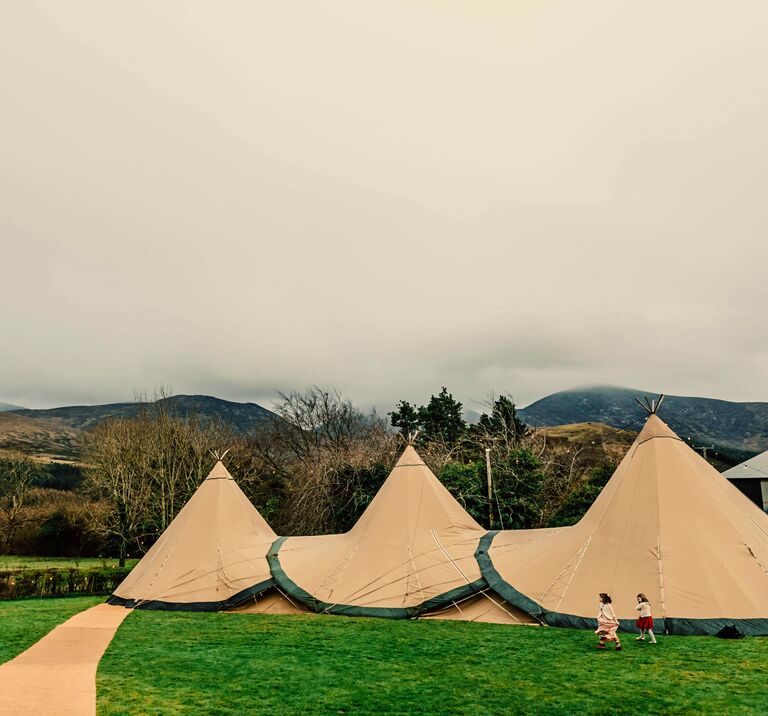 Three tipis stand in a field with the Mourne Mountains behind them, they create a charming outdoor structure perfect for a wedding